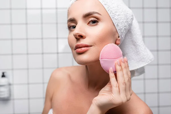 Mujer en toalla en la cabeza usando cepillo de silicona de limpieza en el baño - foto de stock