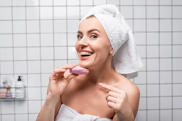 Mujer alegre en toalla en la cabeza apuntando con el dedo a la limpieza de cepillo de silicona en el baño — Stock Photo