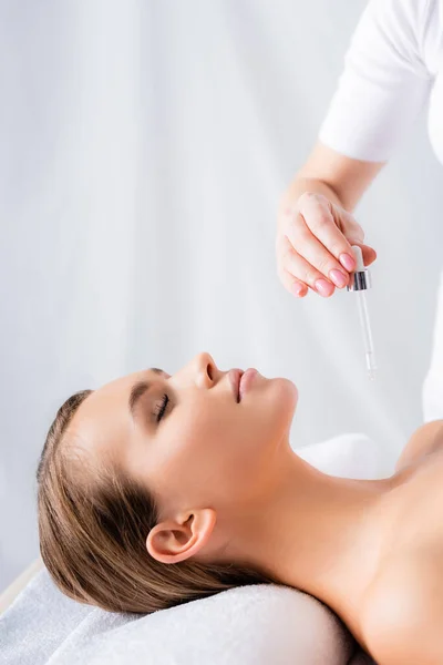 Beautician holding pipette with serum near woman in spa salon — Stock Photo