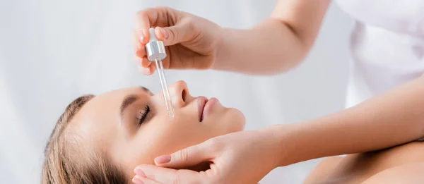 Esthéticienne tenant la pipette et appliquant le sérum sur le visage de la femme dans le salon de spa, bannière — Photo de stock