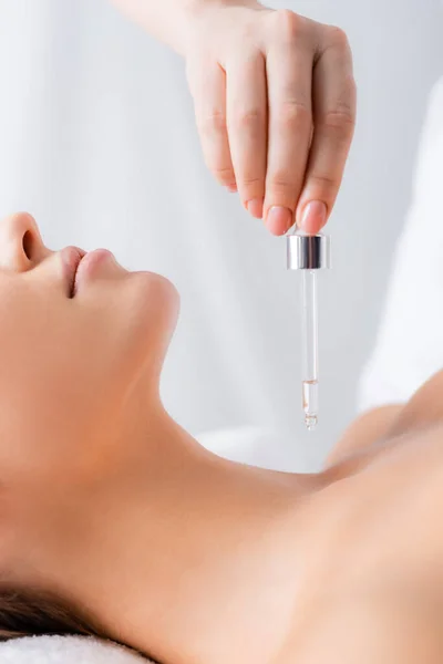 Cropped view of beautician holding pipette with serum near woman in spa salon — Stock Photo