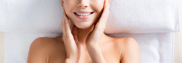 Vista superior da mulher feliz tocando bochechas e deitado na mesa de massagem no salão de spa, banner — Fotografia de Stock