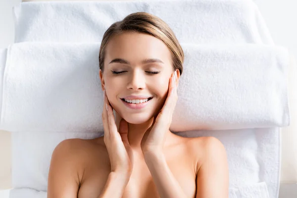 Draufsicht auf freudige Frau mit geschlossenen Augen, die auf Massagetisch im Wellness-Salon liegt — Stockfoto