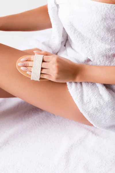 Partial view of woman wrapped in towel exfoliating skin on leg — Stock Photo