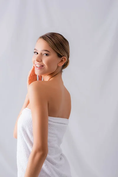 Cheerful young woman wrapped in white towel smiling on white — Stock Photo