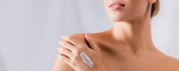 Partial view of young woman with bare shoulders and cream on hand on white, banner — Stock Photo