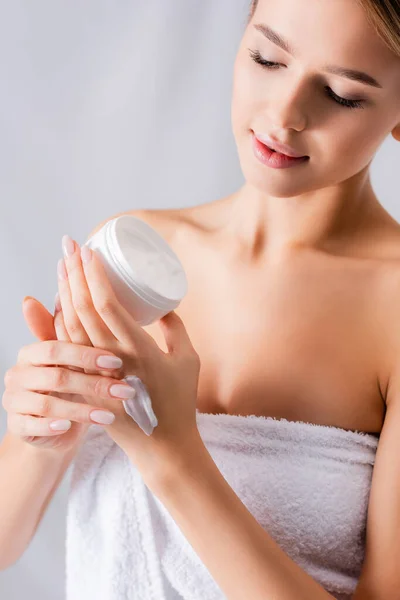 Young woman with bare shoulders holding jar with cream on white — Stock Photo