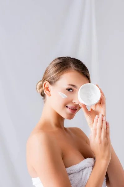 Felice giovane donna con crema sul viso in possesso di vaso e guardando la fotocamera su bianco — Foto stock