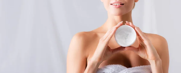 Vista parziale di giovane donna sorridente che tiene il vaso con crema su bianco, striscione — Foto stock