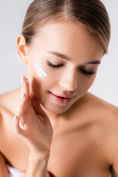 Jeune femme aux épaules nues appliquant crème visage isolé sur blanc — Photo de stock