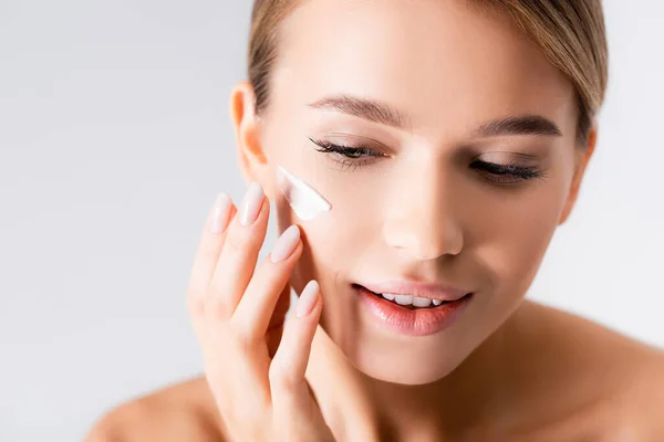 Mujer joven con hombros desnudos aplicando crema hidratante en la cara aislada en blanco — Stock Photo