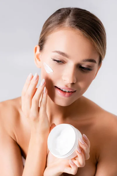 Young woman with bare shoulders holding jar and applying face cream isolated on white — Stock Photo