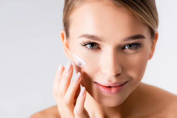 Joyful young woman applying moisturizing cream on face isolated on white — Stock Photo