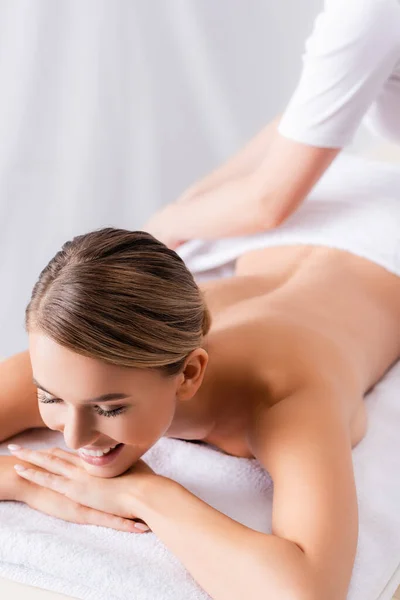 Masajista borrosa ajustando toalla en cliente feliz acostado en mesa de masaje - foto de stock