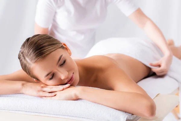 Massagista desfocado ajustando toalha no cliente com os olhos fechados deitado na mesa de massagem — Fotografia de Stock