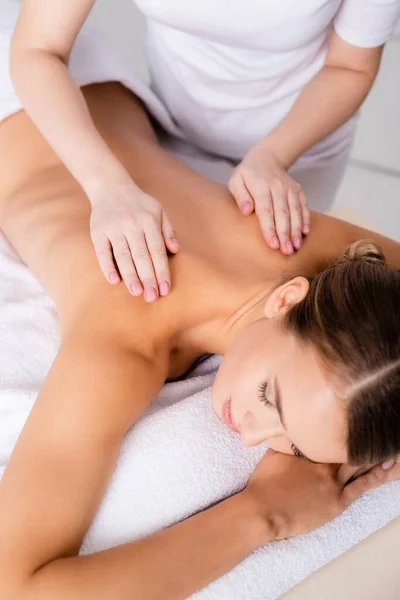 Masajista femenina masajeando la espalda del cliente acostado en la mesa de masaje - foto de stock