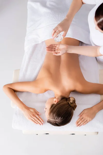 Top view masseur holding glass bottle and pouring massage oil on hand near client — Stock Photo