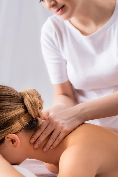 Vista cortada do massagista massageando o pescoço do cliente deitado na mesa de massagem — Fotografia de Stock