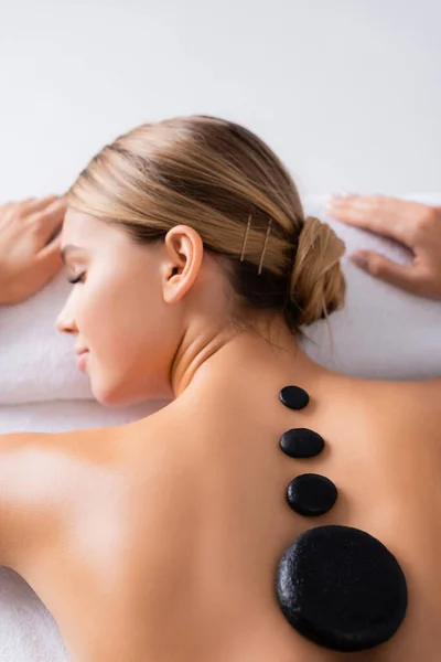 Femme avec les yeux fermés obtenir un massage aux pierres chaudes près de la bougie brûlante dans le salon de spa — Photo de stock