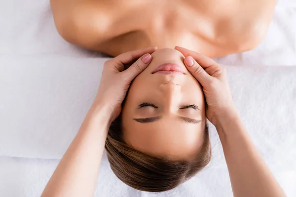 Vista superior de masajista haciendo masaje facial a cliente joven en salón de spa - foto de stock