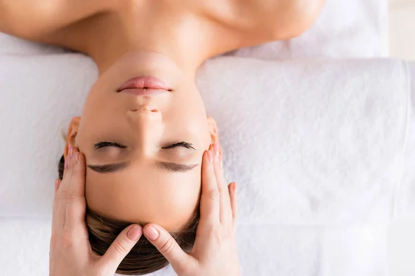 Vista superior de masajista haciendo masaje facial a mujer en salón de spa - foto de stock