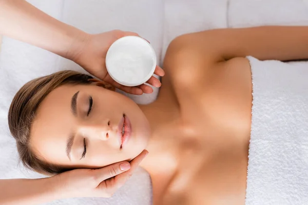 Top view of beautician holding container with face mask near woman on massage table — Stock Photo