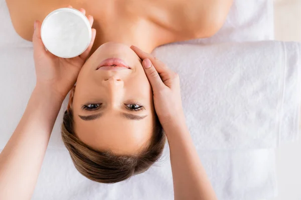 Vue du dessus du récipient de tenue esthéticienne avec masque facial près de la femme sur la table de massage — Photo de stock