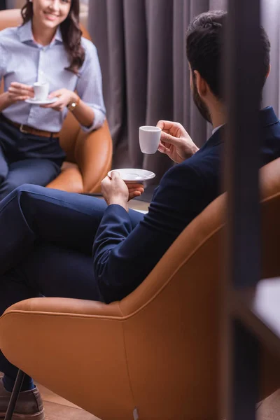 Foyer sélectif de l'homme d'affaires arabe avec tasse de café près partenaire d'affaires souriant dans la zone de salon, au premier plan flou — Photo de stock