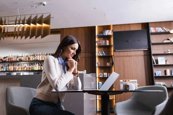 Позитивный фрилансер смотрит на ноутбук, сидя в ресторане — стоковое фото