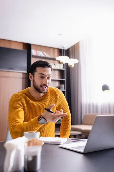 Asombrado árabe freelancer apuntando a la computadora portátil en el restaurante, borrosa primer plano - foto de stock