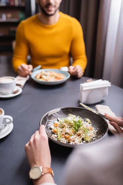 Vue recadrée de la femme tenant des couverts près de la salade et petit ami sur fond flou dans le restaurant — Photo de stock