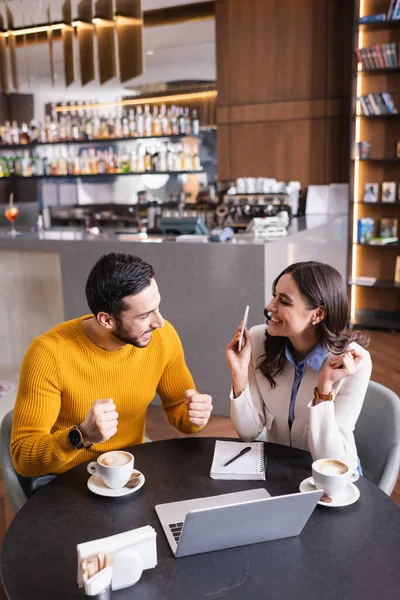 Arabe homme montrant geste oui proche ami avec smartphone, ordinateur portable et café dans le restaurant — Photo de stock