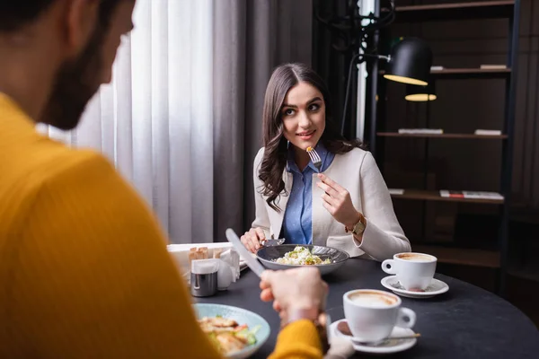 Mujer joven mirando novio en primer plano borrosa cerca de sabrosa ensalada y café en el restaurante - foto de stock