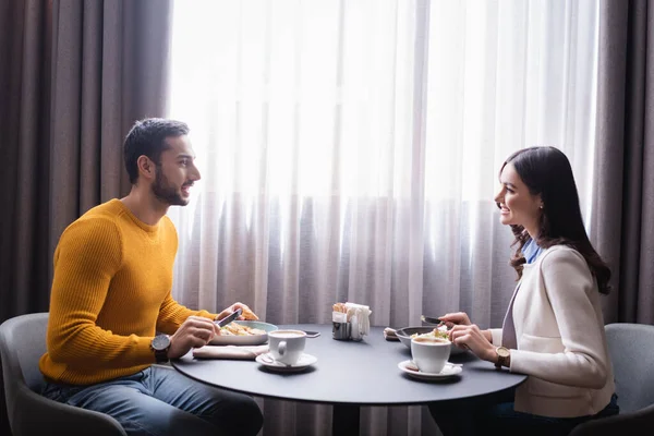 Alegre pareja interracial mirándose mientras cenan en el restaurante - foto de stock