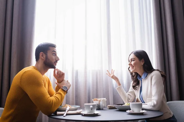 Mujer sonriente hablando con novio árabe cerca de la comida y el café en el restaurante — Stock Photo