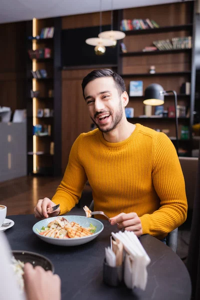 Hombre árabe alegre cenando con su novia en primer plano borroso en el restaurante moderno - foto de stock
