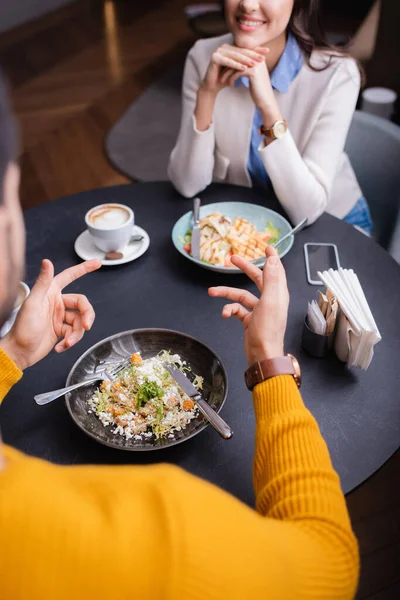 Vista recortada del hombre señalando con el dedo cerca de la ensalada y la novia sonriente sobre fondo borroso en el restaurante - foto de stock