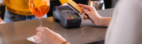 Vue recadrée de la femme payant avec carte de crédit près de cocktail et barman sur fond flou, bannière — Photo de stock