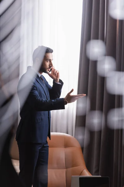 Homem de negócios árabe apontando com a mão enquanto fala no celular no restaurante — Fotografia de Stock