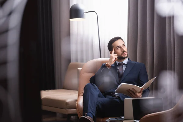 Nachdenklicher arabischer Geschäftsmann mit Papiermappe sitzt in Restaurant neben Laptops — Stockfoto
