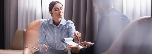 Donna d'affari con quaderno che punta agli appunti vicino al partner arabo in primo piano sfocato nel ristorante, banner — Foto stock