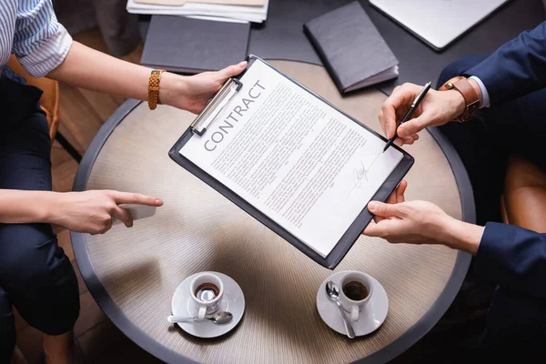 Vue recadrée de femme d'affaires pointant vers le contrat tout partenaire chantant dans le restaurant — Photo de stock