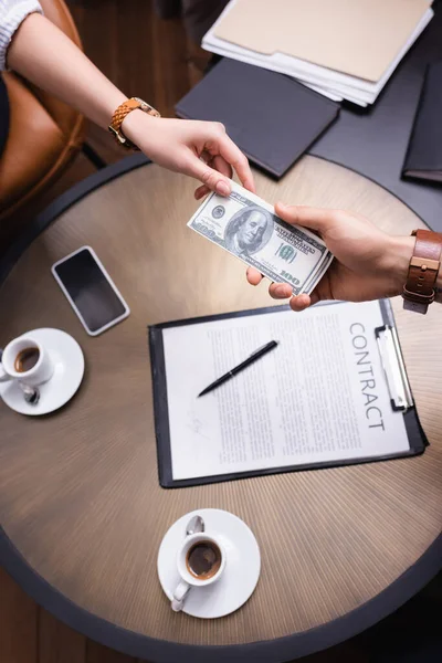 Vista recortada de gente de negocios sosteniendo dólares cerca de contrato y café en restaurante - foto de stock