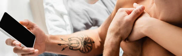 Cropped view of woman hugging shirtless man with smartphone, banner — Stock Photo