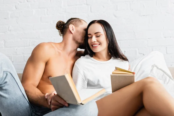 Homme sexy embrasser petite amie souriante avec livre sur le premier plan flou — Photo de stock