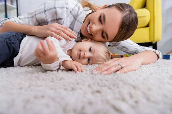 Поверхностный уровень счастливой матери с маленьким сыном, лежащим на ковре дома, размытый передний план — стоковое фото