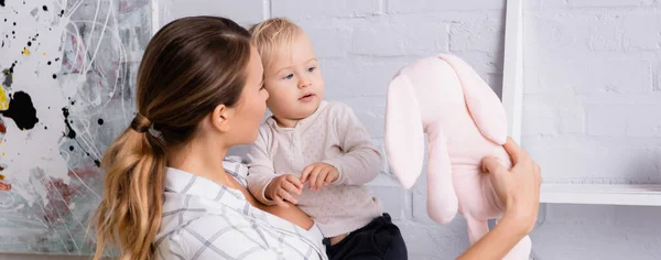 Junge Frau zeigt Spielzeughase dem Kind zu Hause, Transparent — Stockfoto