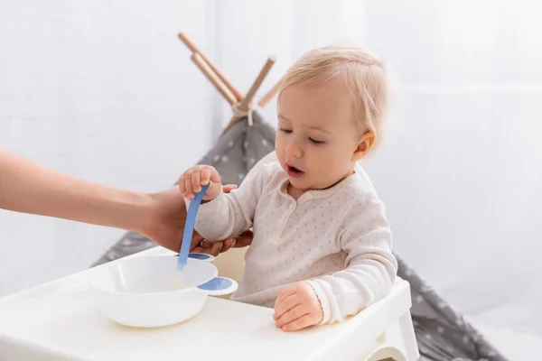 Mother helping little son holding spoon near bowl with puree — Stock Photo
