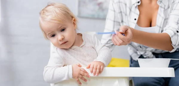 Toddler boy turning away from spoon with puree in hand of mother, blurred background, banner — Stock Photo