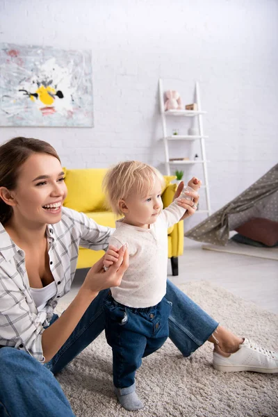 Excited woman supporting toddler son walking at home — Stock Photo